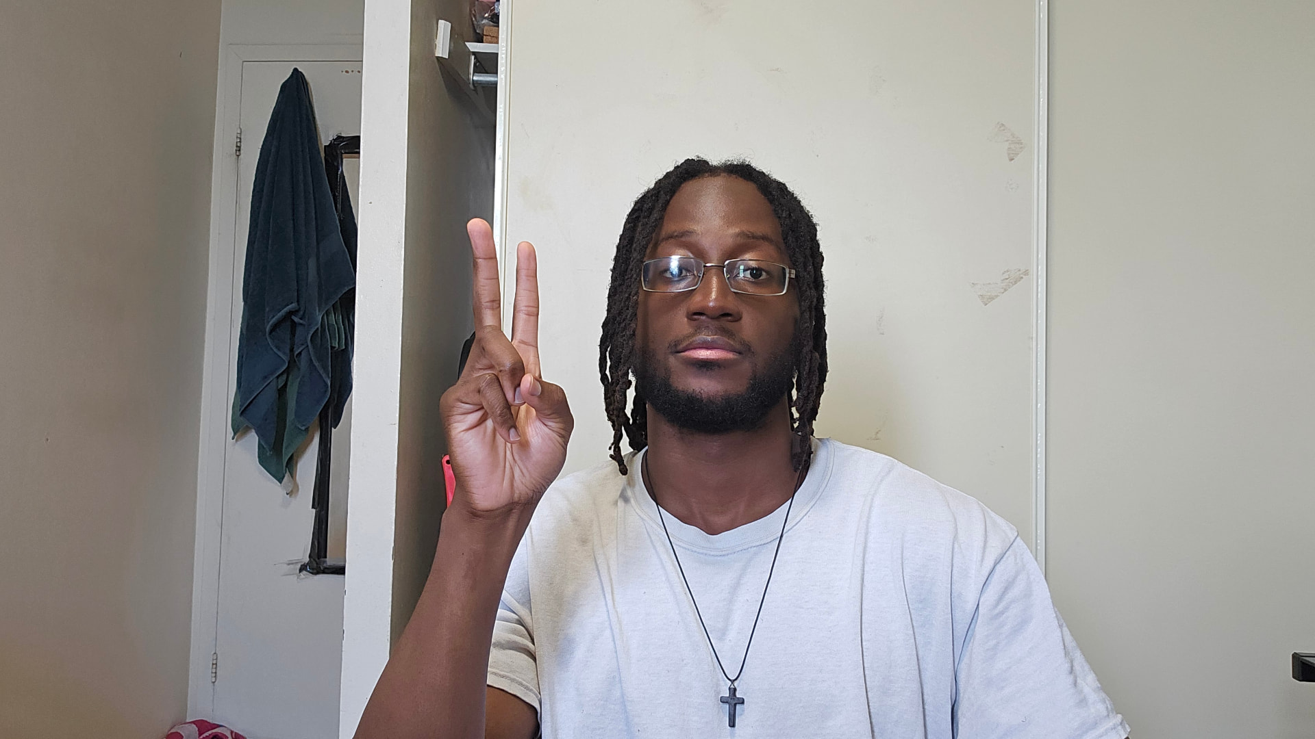 Mike in a white t-shirt and glasses, holding up a peace sign indoors